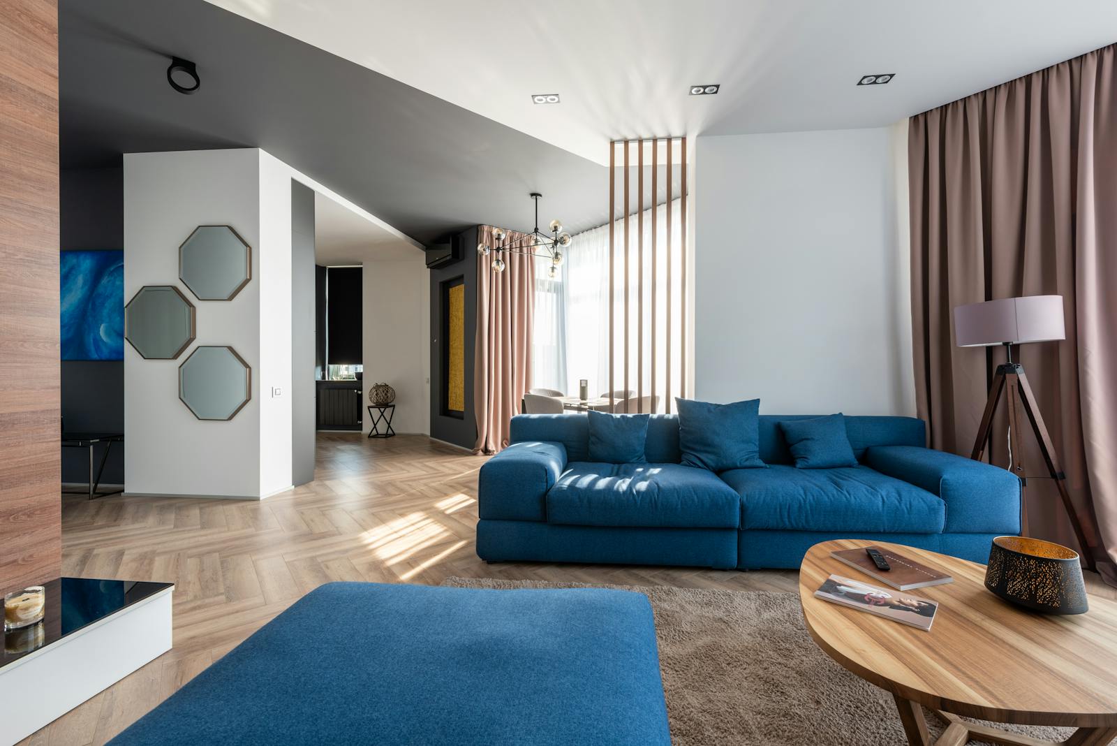 Intérieur d'un appartement spacieux avec canapé bleu et pouf près d'une table en bois posée sur un tapis près du mur avec des décorations élégantes