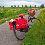 Un vélo chargé de bagages rouges et un panier, posé sur une route