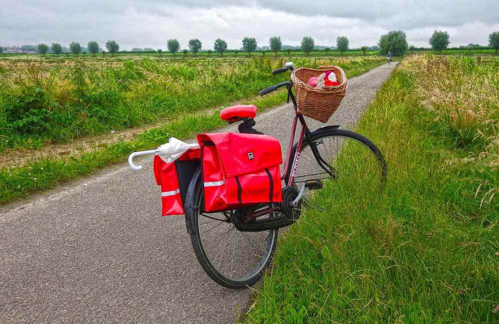 Un vélo chargé de bagages rouges et un panier, posé sur une route