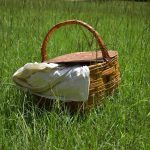 Un panier en osier repose sur l'herbe avec une nappe blanche