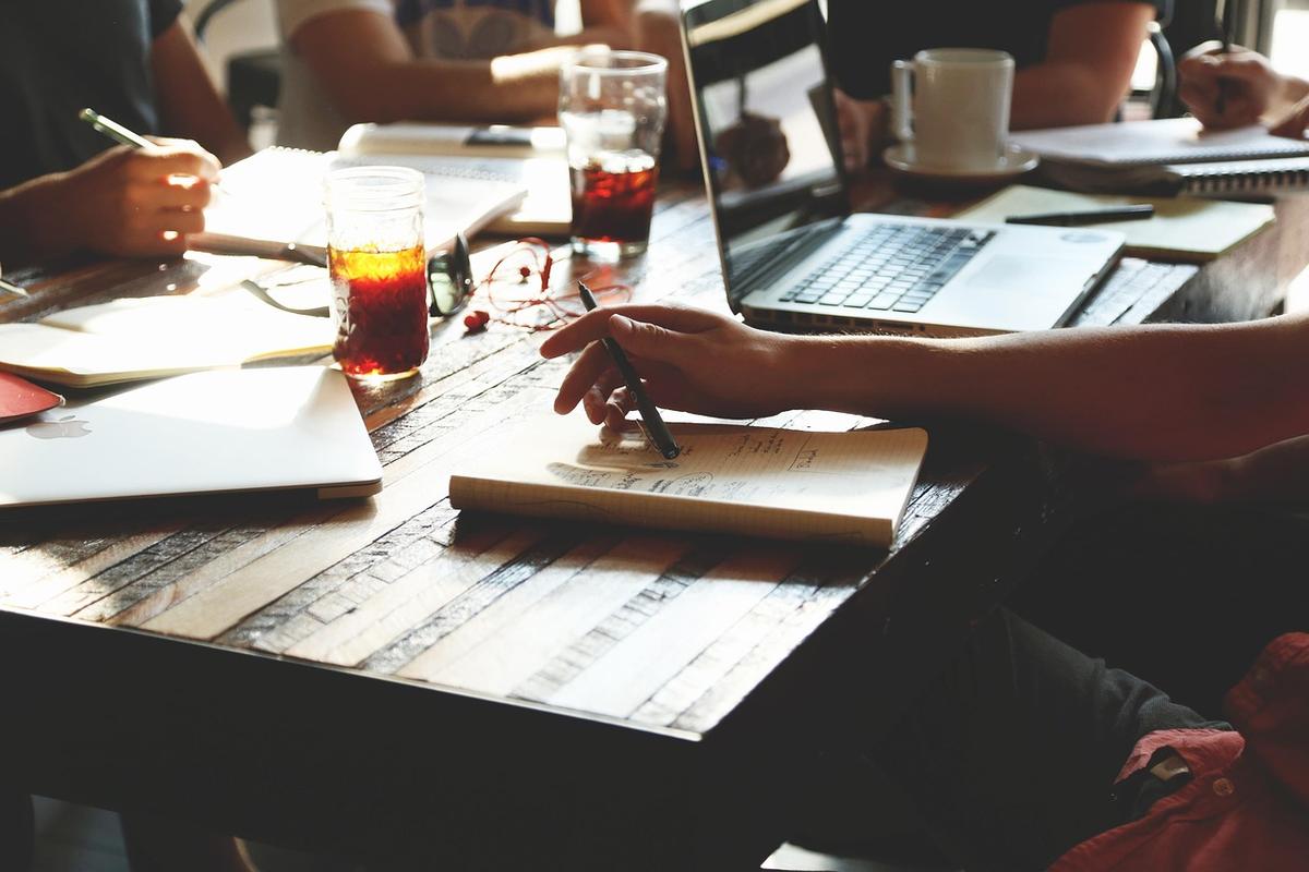 Des mains écrivent dans des carnets sur une table avec ordinateur et boissons Des mains écrivent dans des carnets sur une table avec ordinateur et boissons