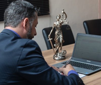 Homme écrivant sur un papier devant un ordinateur portable avec une statue de justice à côté