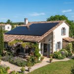 Toit de maison individuelle française avec panneaux solaires photovoltaïques, ciel dégagé, jardin