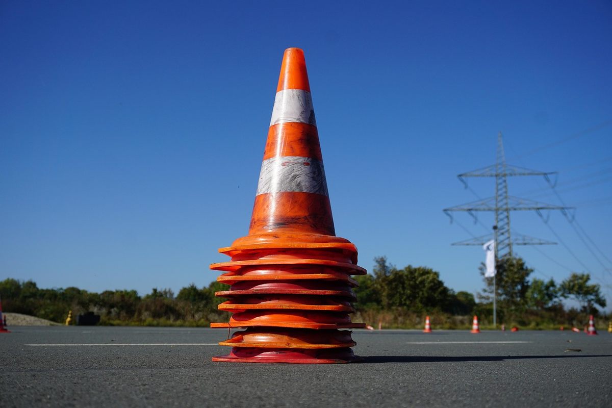 Un cône orange empilé sur une route ciel bleu pylône électrique