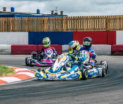 Trois karts dérapent en virage sur circuit, pilotes en casques colorés