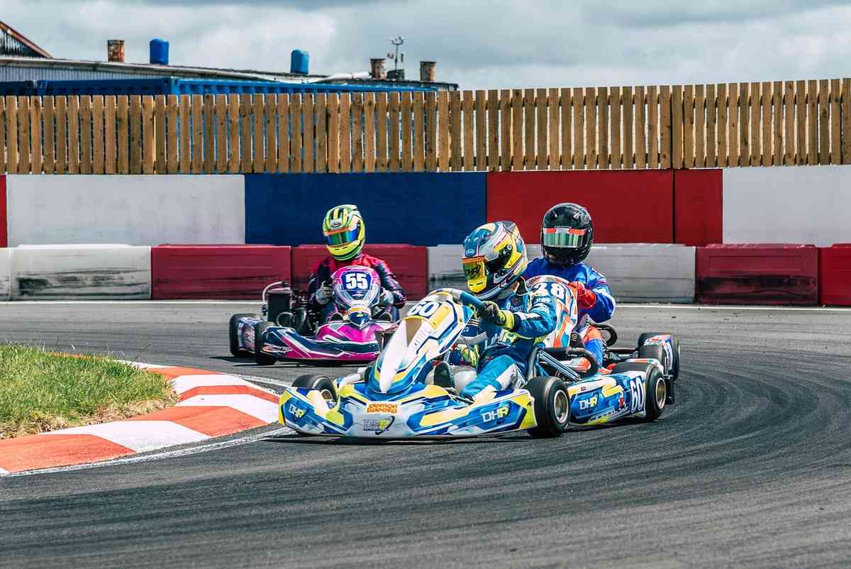 Trois karts dérapent en virage sur circuit, pilotes en casques colorés